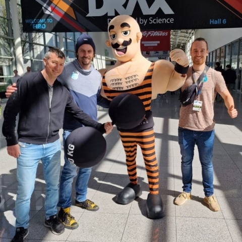 Trainerteam mit einem Gewichtsheber-Maskottchen bei der größten Fitnessmesse Europas in Köln