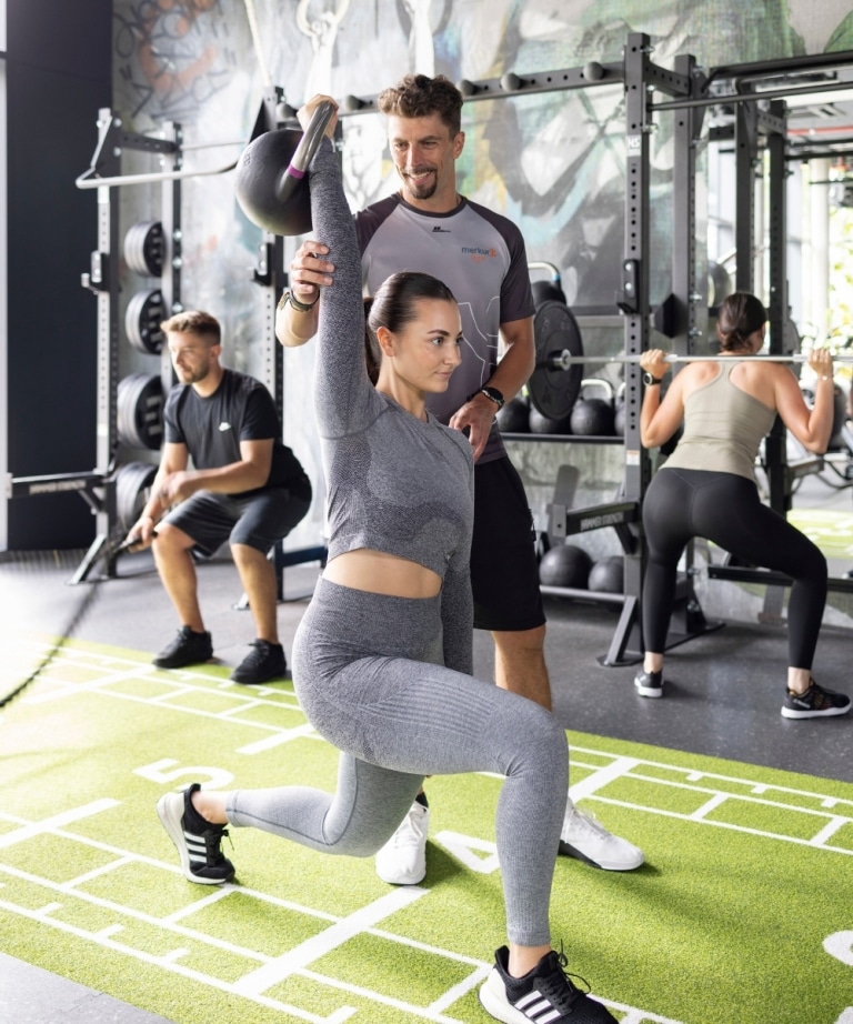 Functional Workout bei dem Coach Stefan einer Dame bei ihrer Übung hilft und im Hintergrund eine Dame und ein Herr ihr Workout machen